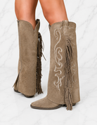 Tan suede boots with fringe and white embroidery on a light gray background